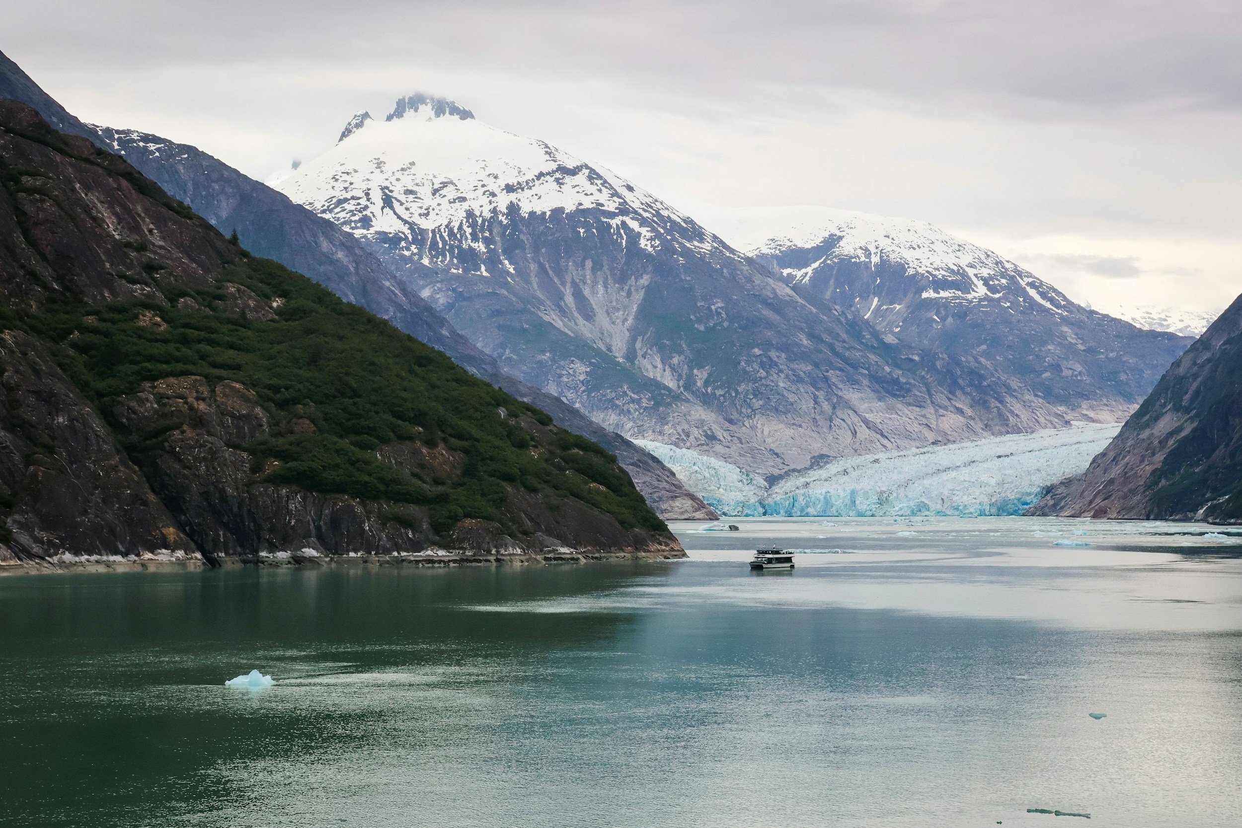 A small ship cruising calm waters past forested mountains in Alaska's Inside Passage
