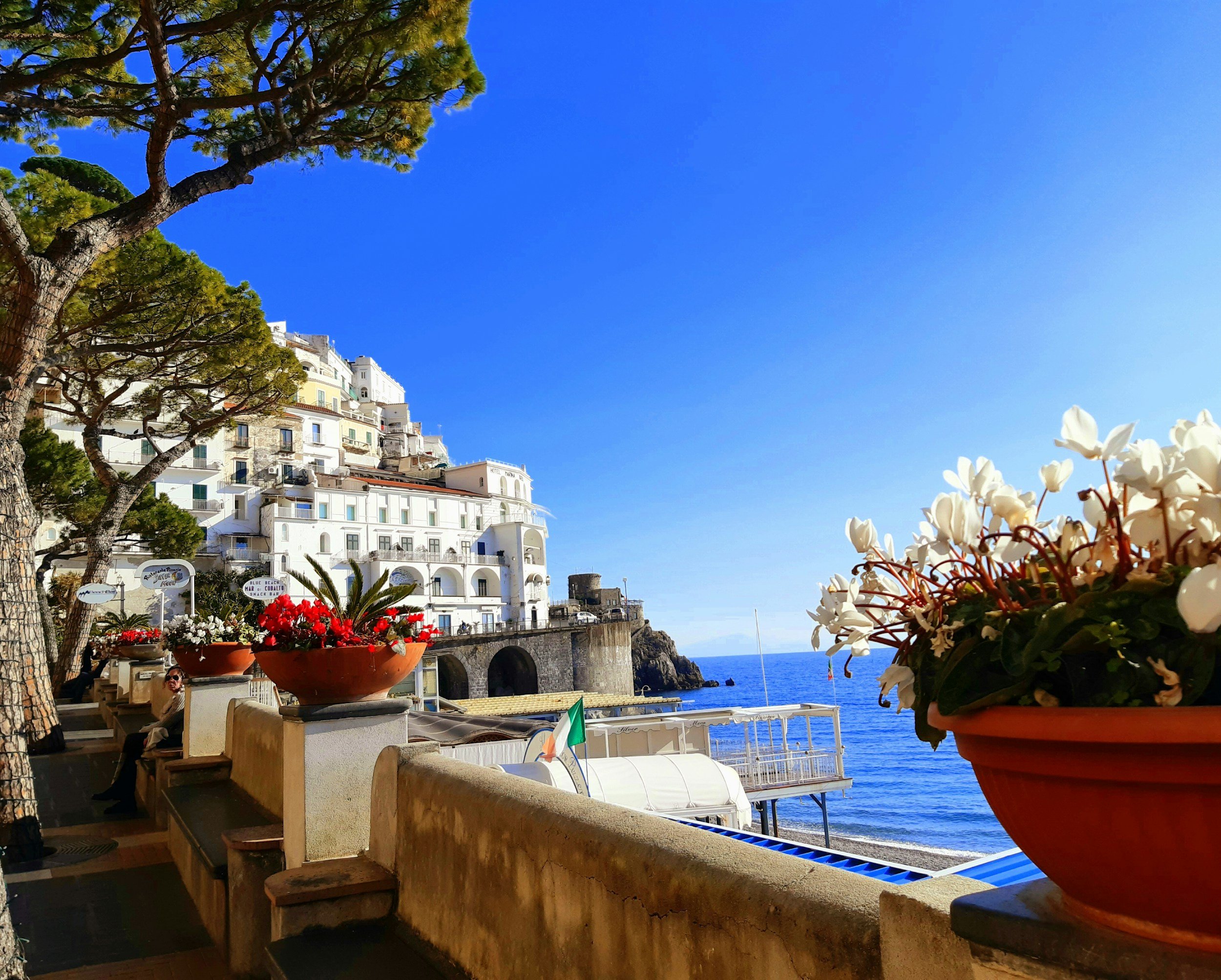 A flower-lined hotel terrace above the sea with white buildings on the cliff