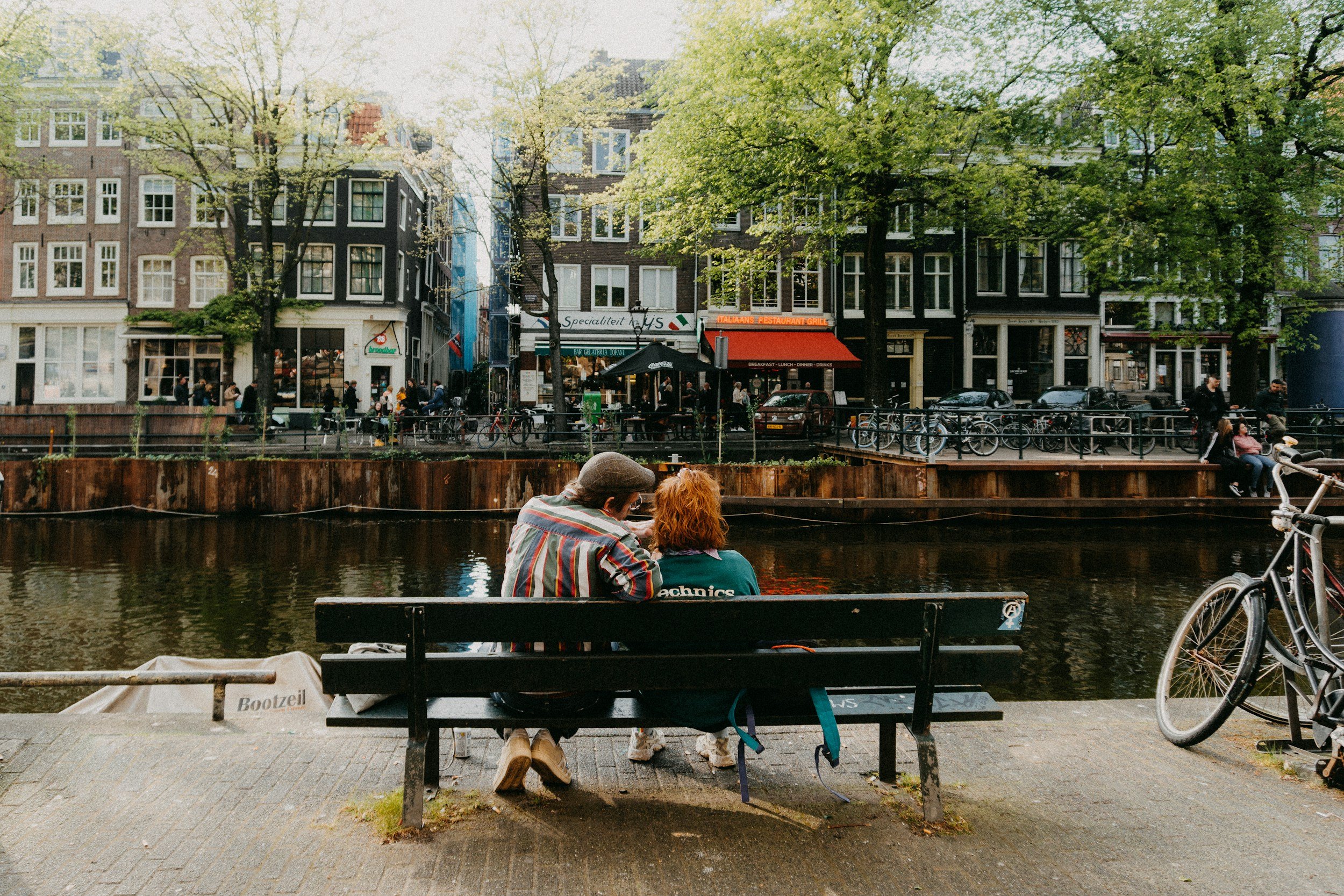 A couple on a bench beside an Amsterdam canal, a bicycle leaning nearby