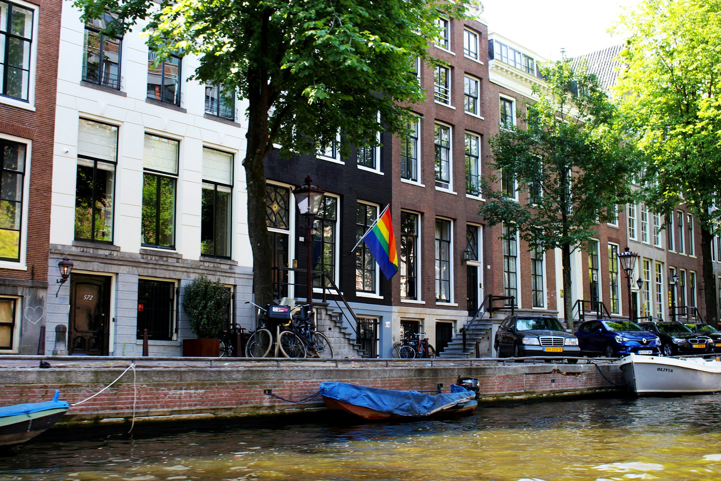 A canal house with a rainbow flag above a boat-lined Amsterdam canal