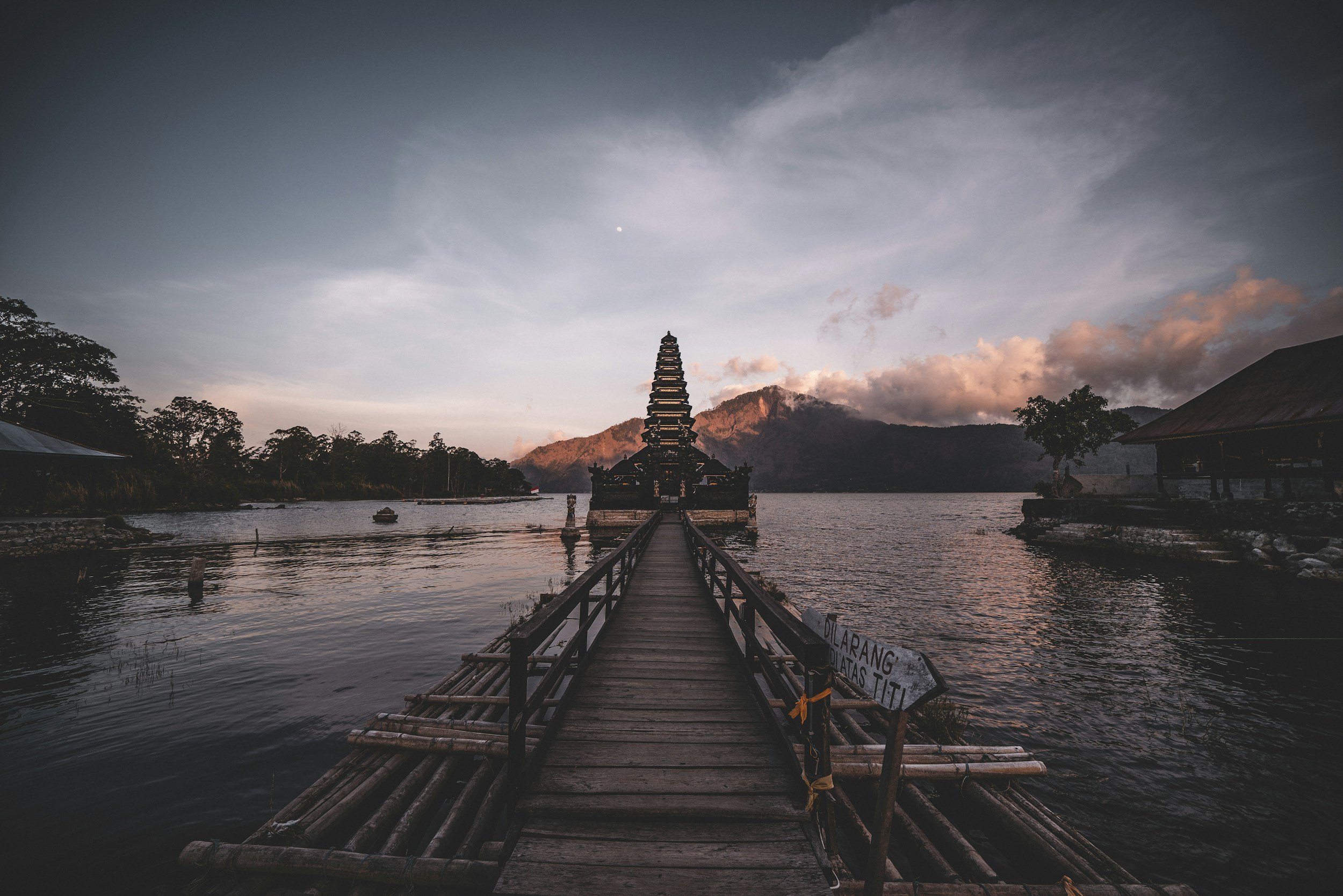 A wooden pier leading to a tiered lake temple under a dusk sky