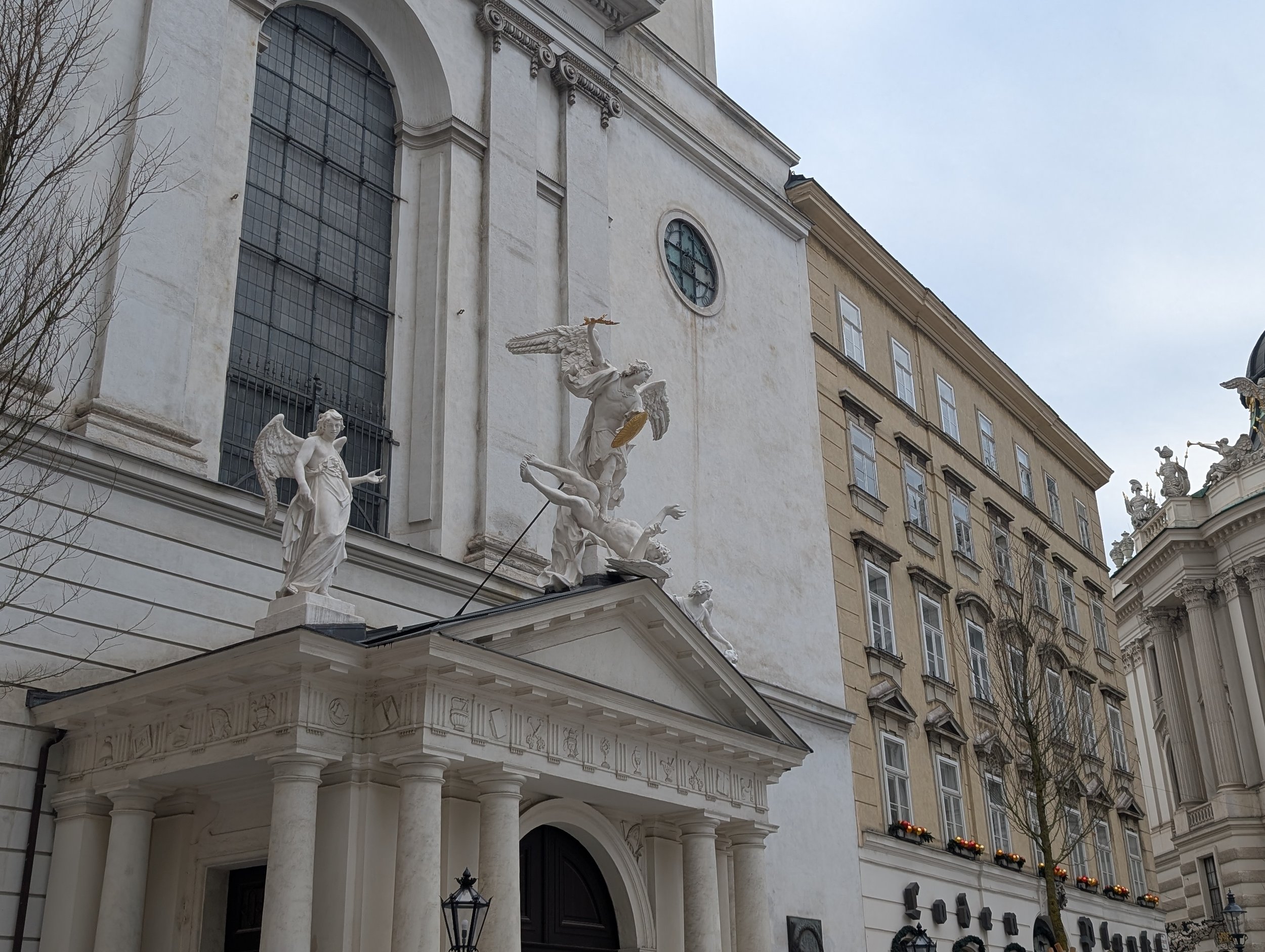 The white facade of St. Michael's Church with its sculpted angels, beside the Hofburg