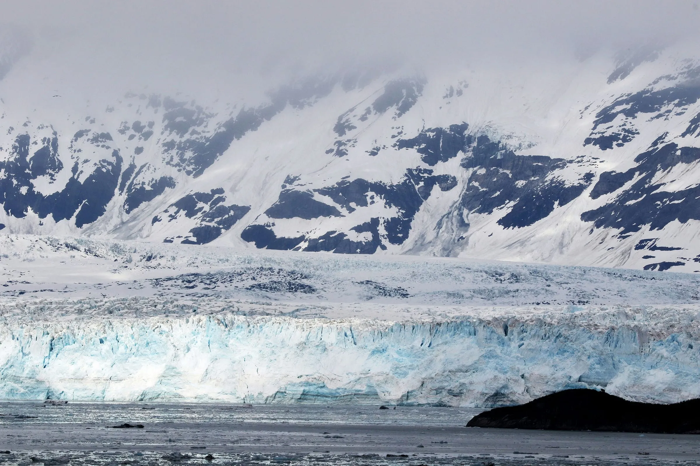 A tidewater glacier meeting the sea beneath snowy peaks in Glacier Bay, Alaska.
